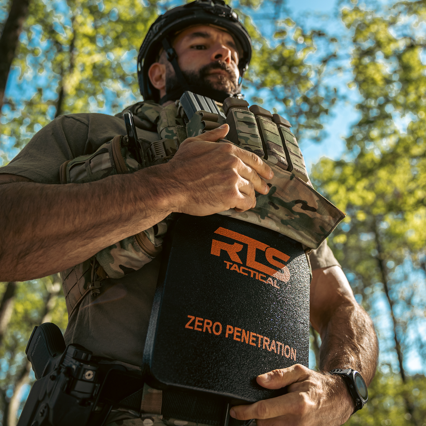 Man in tactical gear adjusts a vest, holding armor plate.