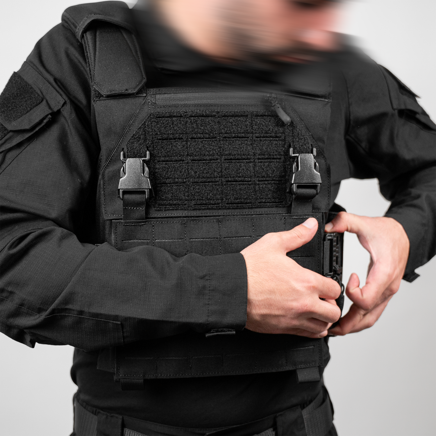A man in a black tactical uniform adjusts his armored vest